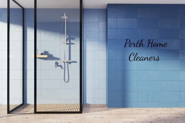 A shower room with blue tiled walls. The sun is shining through the unseen windows on the left. The shower walls are clear. The words Perth Home Cleaners are in black on the wall
