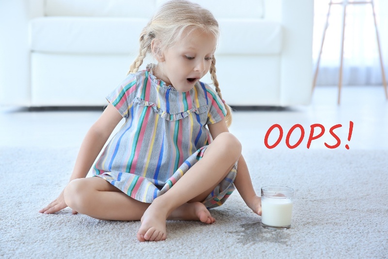 young girl in a striped dress looking in shock at the milk spilled on the carpet