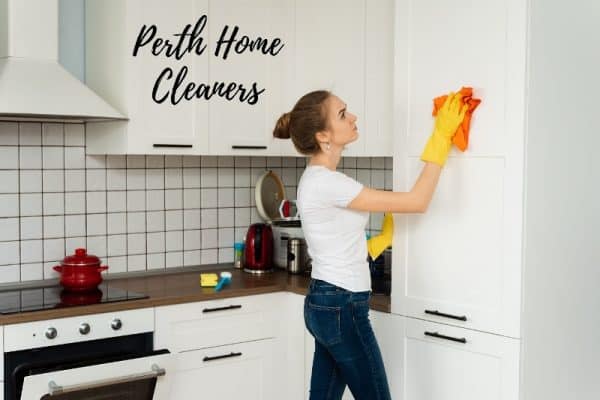 a woman with yellow gloves wiping down a kitchen cupboard